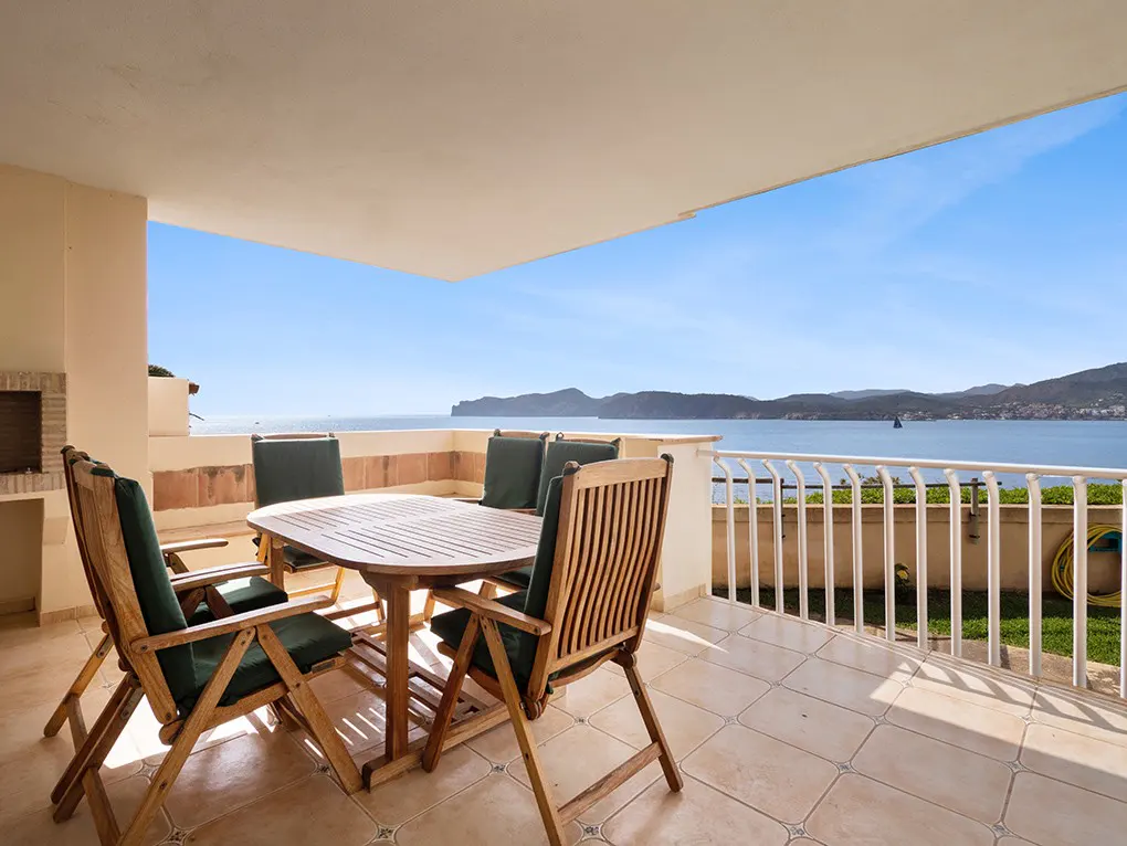 Outdoor patio with wood table and chairs overlooking the ocean on a sunny day.