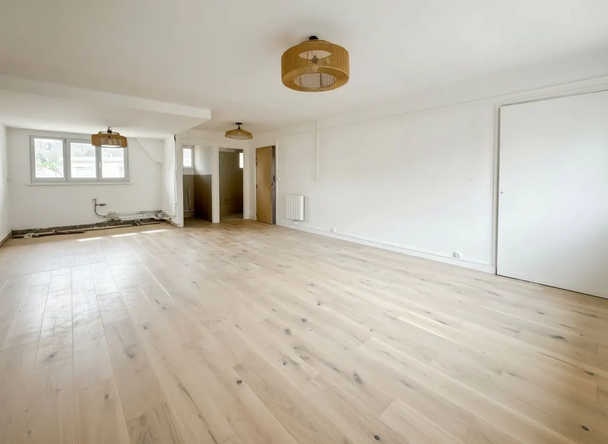 Bright, empty room with light wood floors, white walls, and woven pendant lights. A window and doorway are visible in the background.