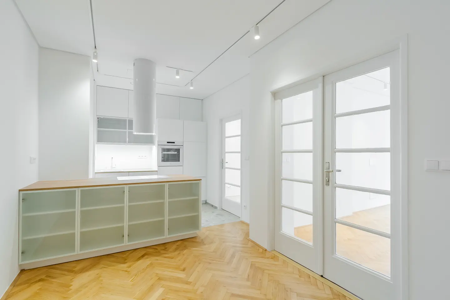 Bright, modern kitchen with white cabinets, wood floors, and glass-paneled doors. Track lighting illuminates the space.
