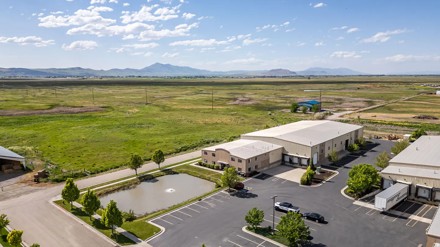 Aerial view of a commercial property with a pond, parking lot, and loading docks against a mountain backdrop.