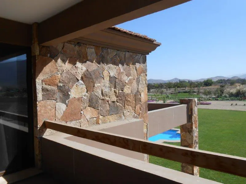 Balcony view of a green lawn, pool, and distant mountains. Stone wall and brown railing frame the scene.