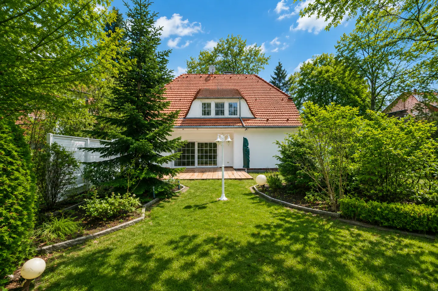 A white house with a red tile roof is surrounded by green trees and a lawn under a blue sky.
