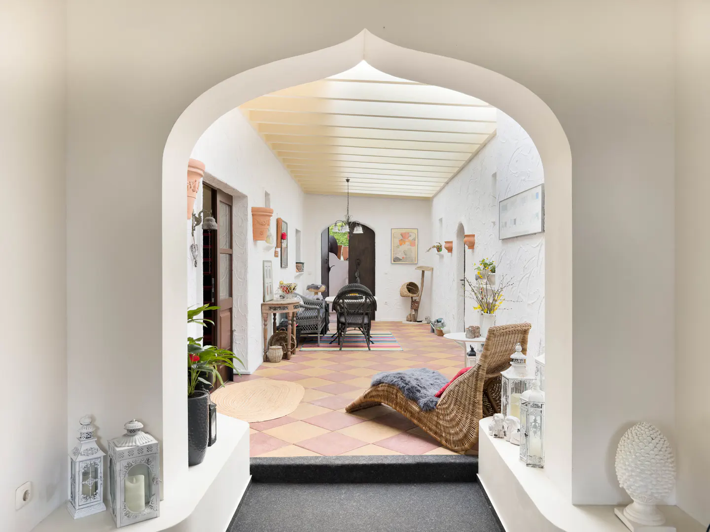 View through a white archway into a sunroom with wicker furniture and a checkered tile floor.