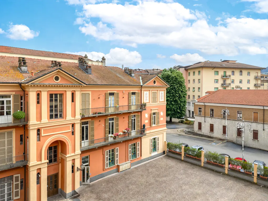 Exterior view of a peach-colored building with balconies and brown shutters, overlooking a courtyard and street with other buildings.