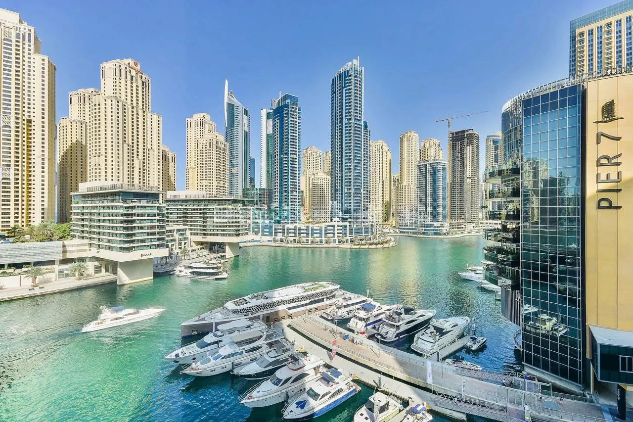 Dubai Marina view with yachts docked in turquoise water, surrounded by modern skyscrapers under a clear blue sky.