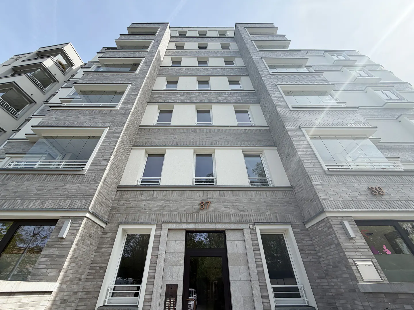 Low angle view of a gray brick apartment building with glass balconies and the number 37 above the entrance.