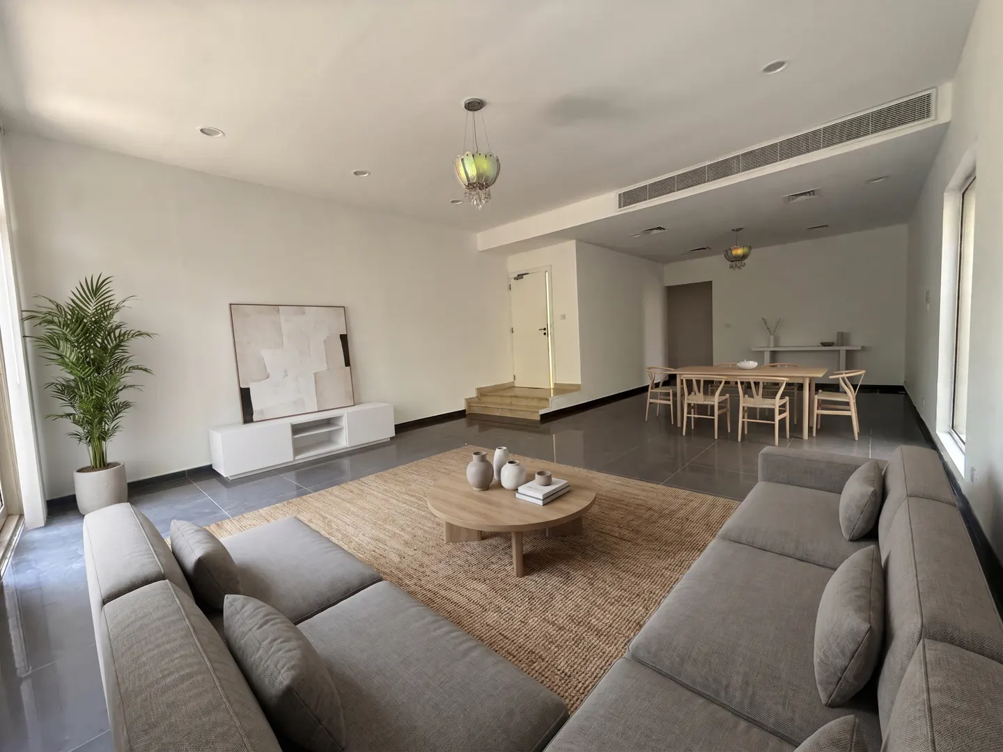 A bright, open-plan living and dining area with a gray sectional sofa, round coffee table on a jute rug, and a dining table with chairs.