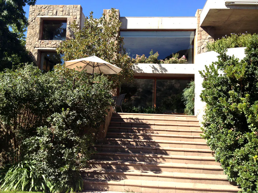 Exterior view of a modern stone house with large windows, a patio umbrella, and stone steps leading up to the entrance.