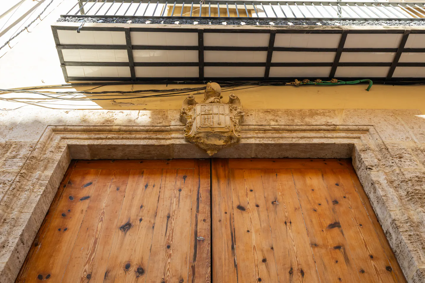 Low angle shot of a wooden door with a stone frame and a coat of arms above it. A balcony is visible above.