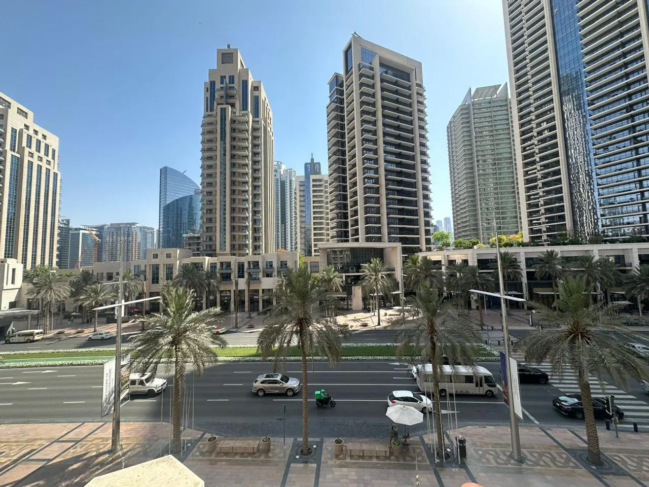 Cityscape view of Dubai with tall buildings, palm trees, and traffic on a sunny day.
