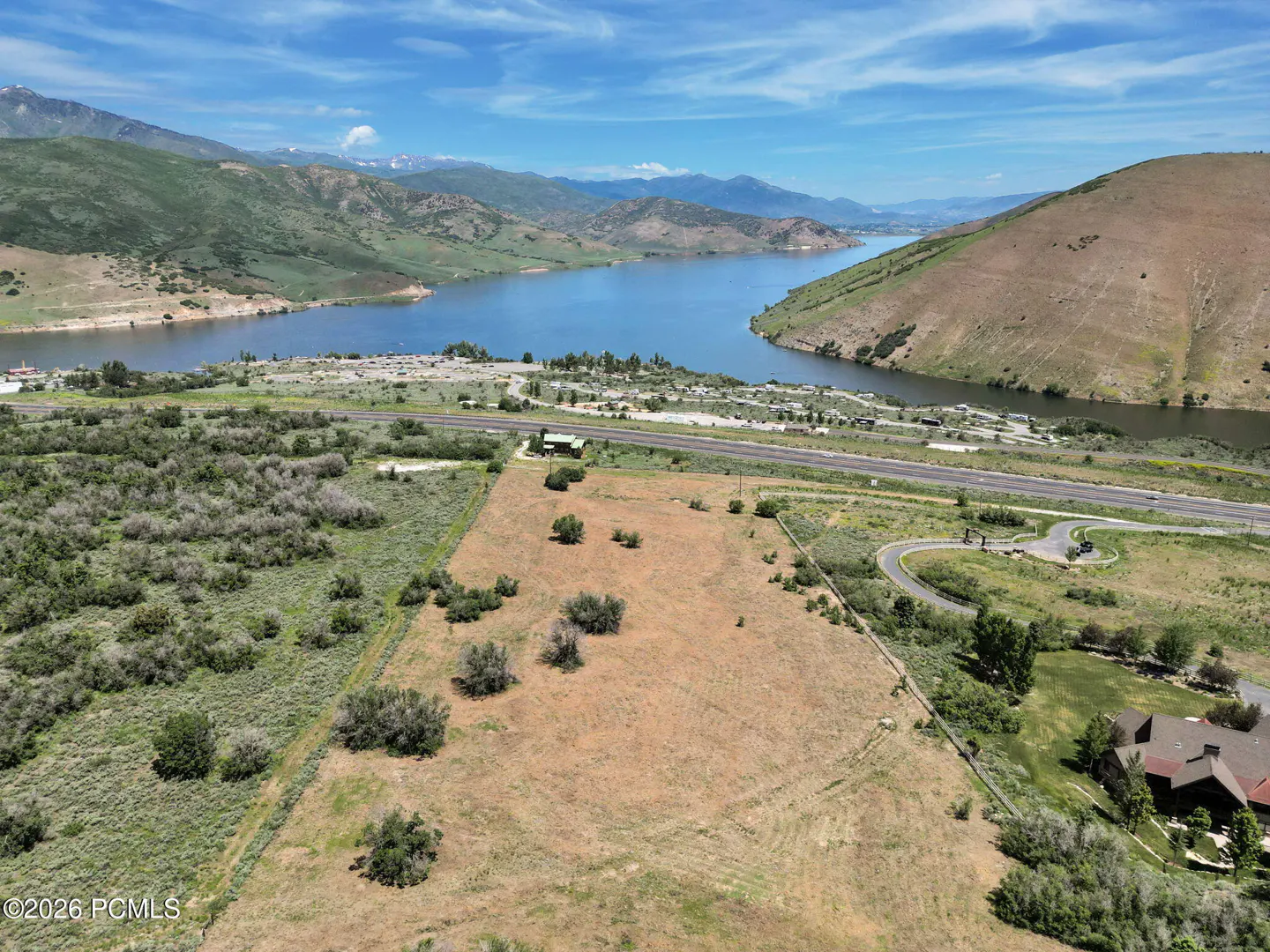 Aerial view of a large, vacant lot with a lake and mountains in the background on a sunny day.