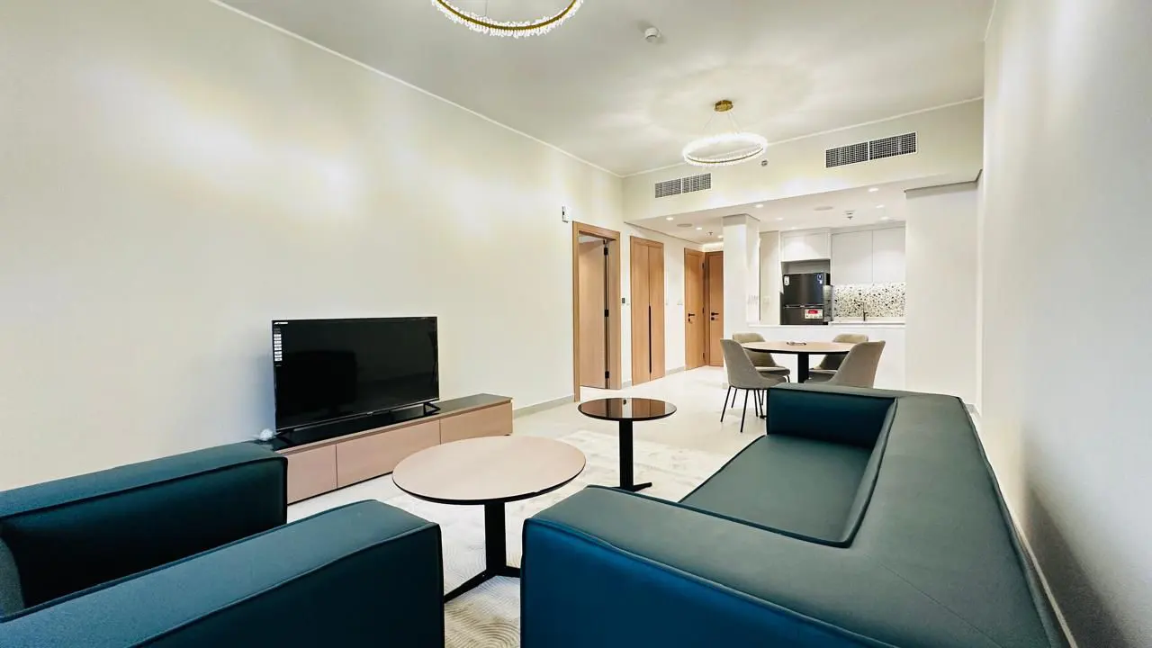 A modern apartment living room with a blue sofa, TV, and dining area.