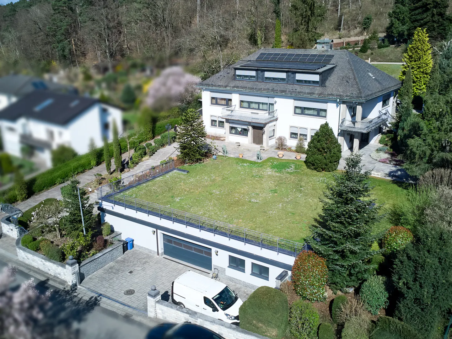Aerial view of a large, white two-story house with solar panels, a green roof on the garage, and a white van parked in the driveway.