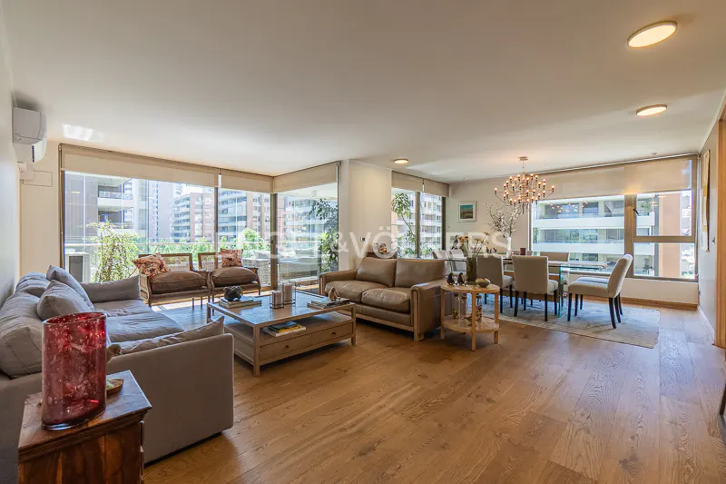 Bright, open-concept living and dining area with hardwood floors, large windows, and city views. Gray sofa and brown leather couch.
