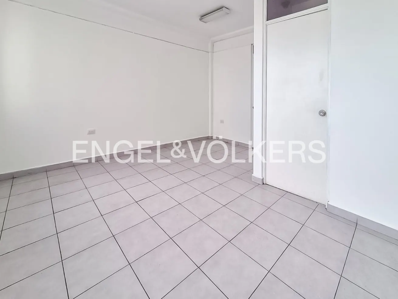 Empty room with white walls, gray tile floor, and a white door. Engel & Volkers logo is superimposed on the image.