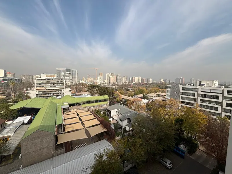 Cityscape view with buildings, trees, and a blue sky with wispy clouds. A green-roofed building is in the foreground.