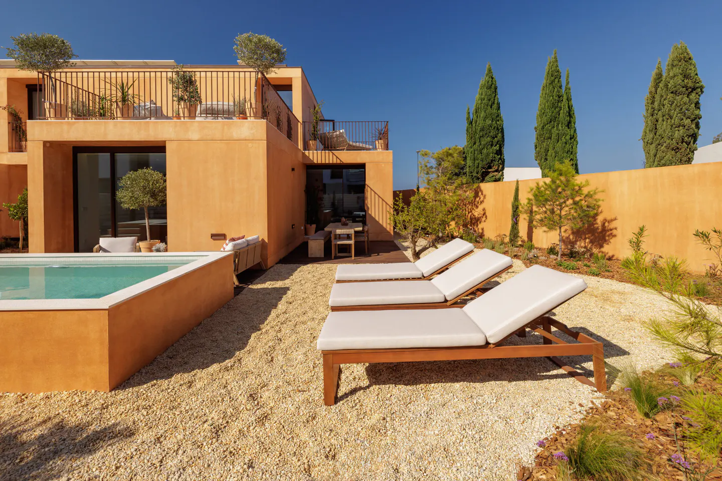A modern orange house with a pool and lounge chairs in the backyard under a clear blue sky.
