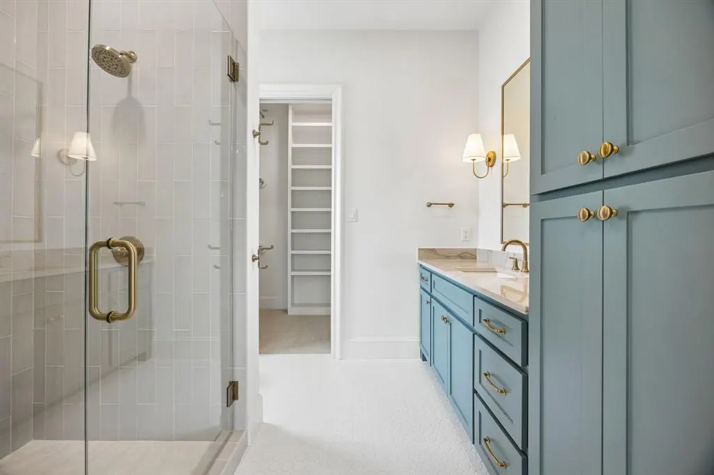 Bathroom with glass shower, blue vanity with gold hardware, marble countertop, and walk-in closet.
