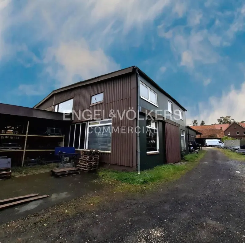 Exterior of a brown and green commercial building with the Engel & Völkers logo. Pallets and metal racks are visible outside.