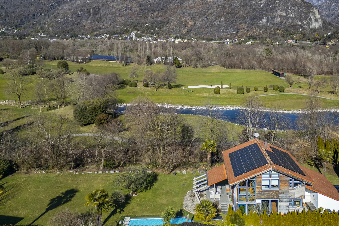 Aerial view of a modern house with solar panels, a pool, and a golf course in the background.