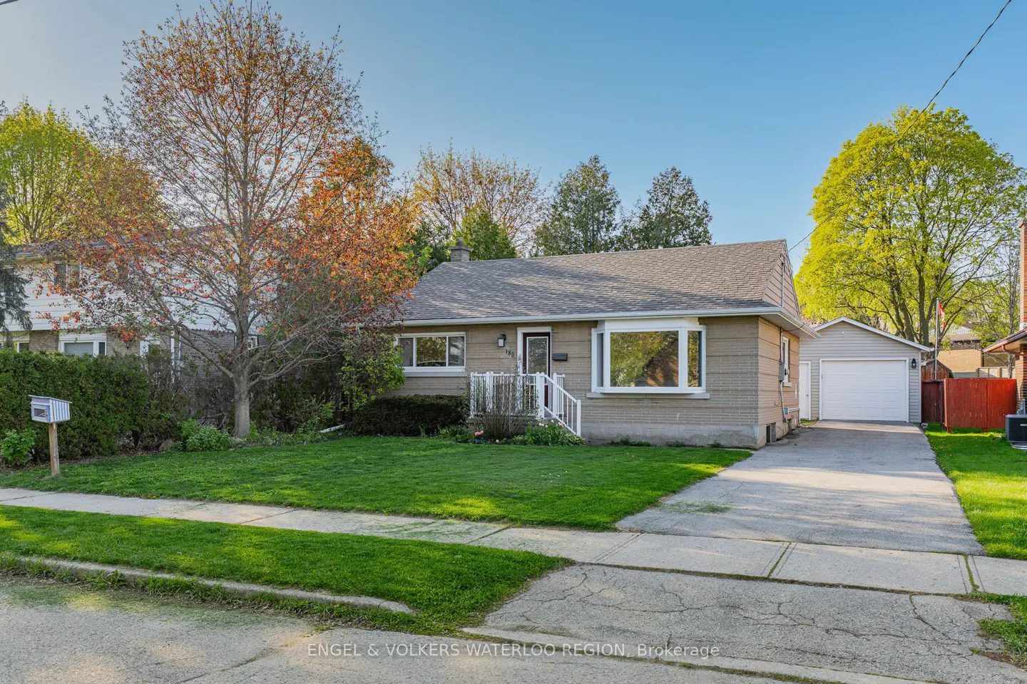 A single-story beige house with a gray roof, green lawn, and a detached garage on a sunny day.