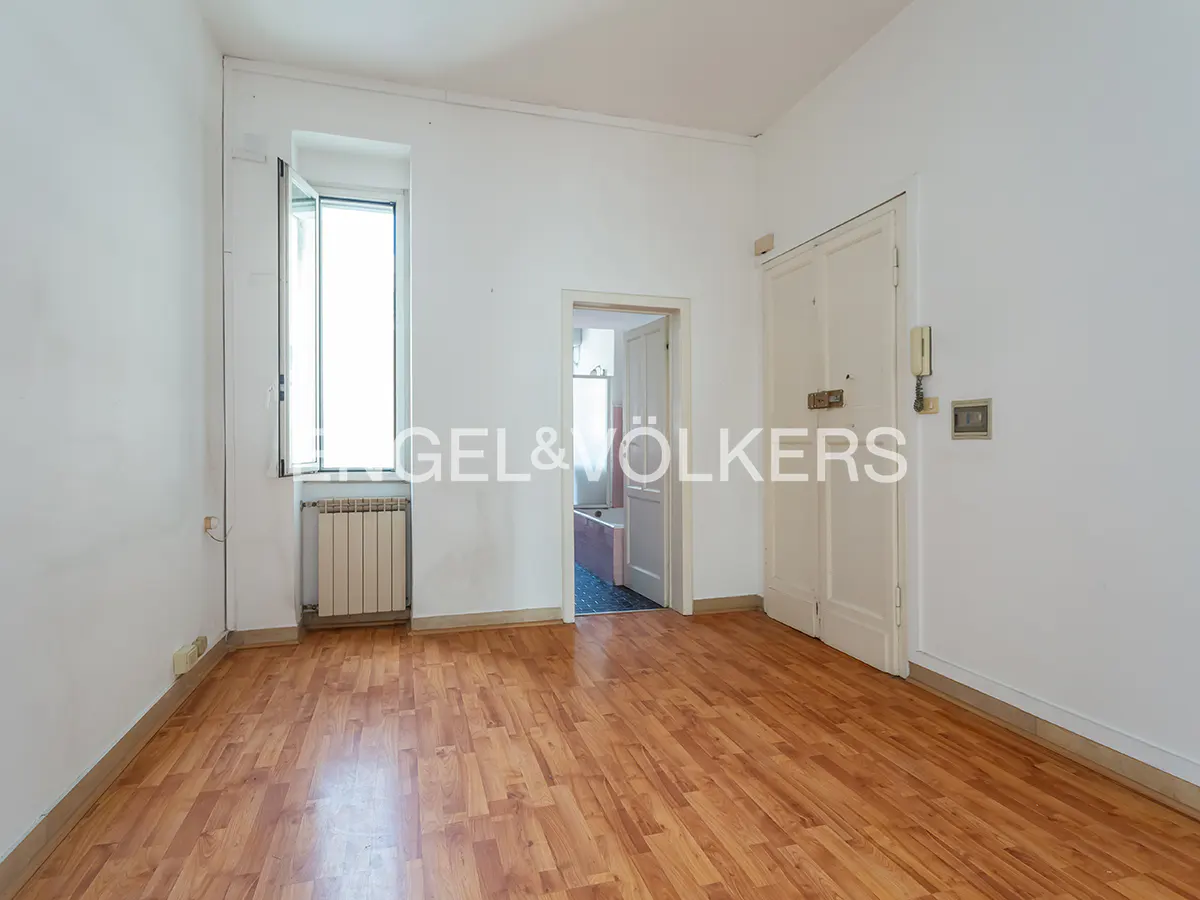 Empty room with wood floors, white walls, a window with a radiator, and a doorway leading to a bathroom.