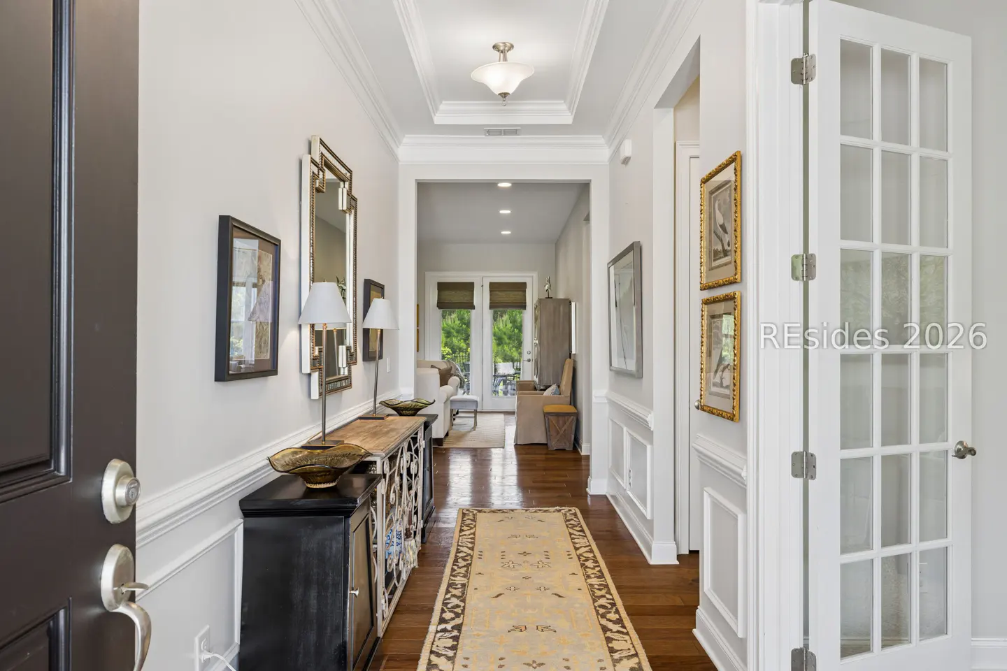 Bright hallway with hardwood floors, a long patterned runner, console table, mirror, and a view into a sunlit living area.