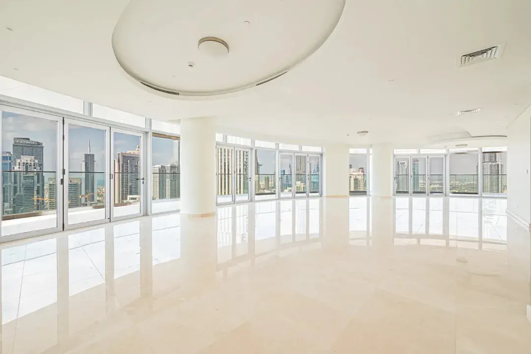 Bright, empty room with beige tile floors and floor-to-ceiling windows showing a city skyline.