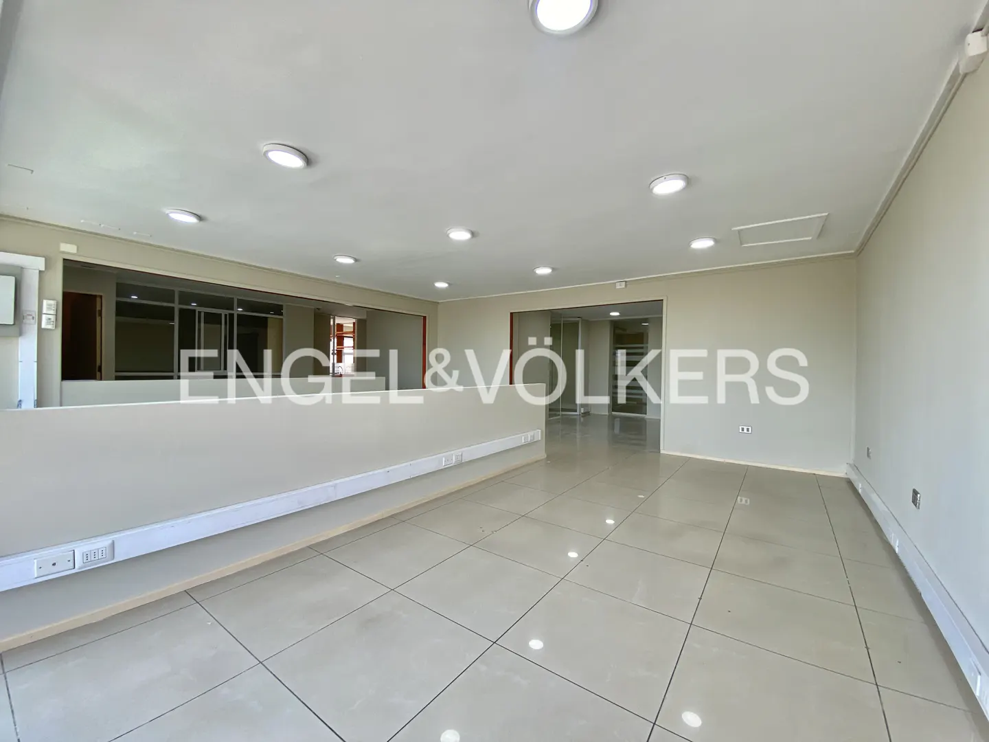 Empty office space with white walls, tile floor, and recessed lighting. Engel & Völkers logo is visible.