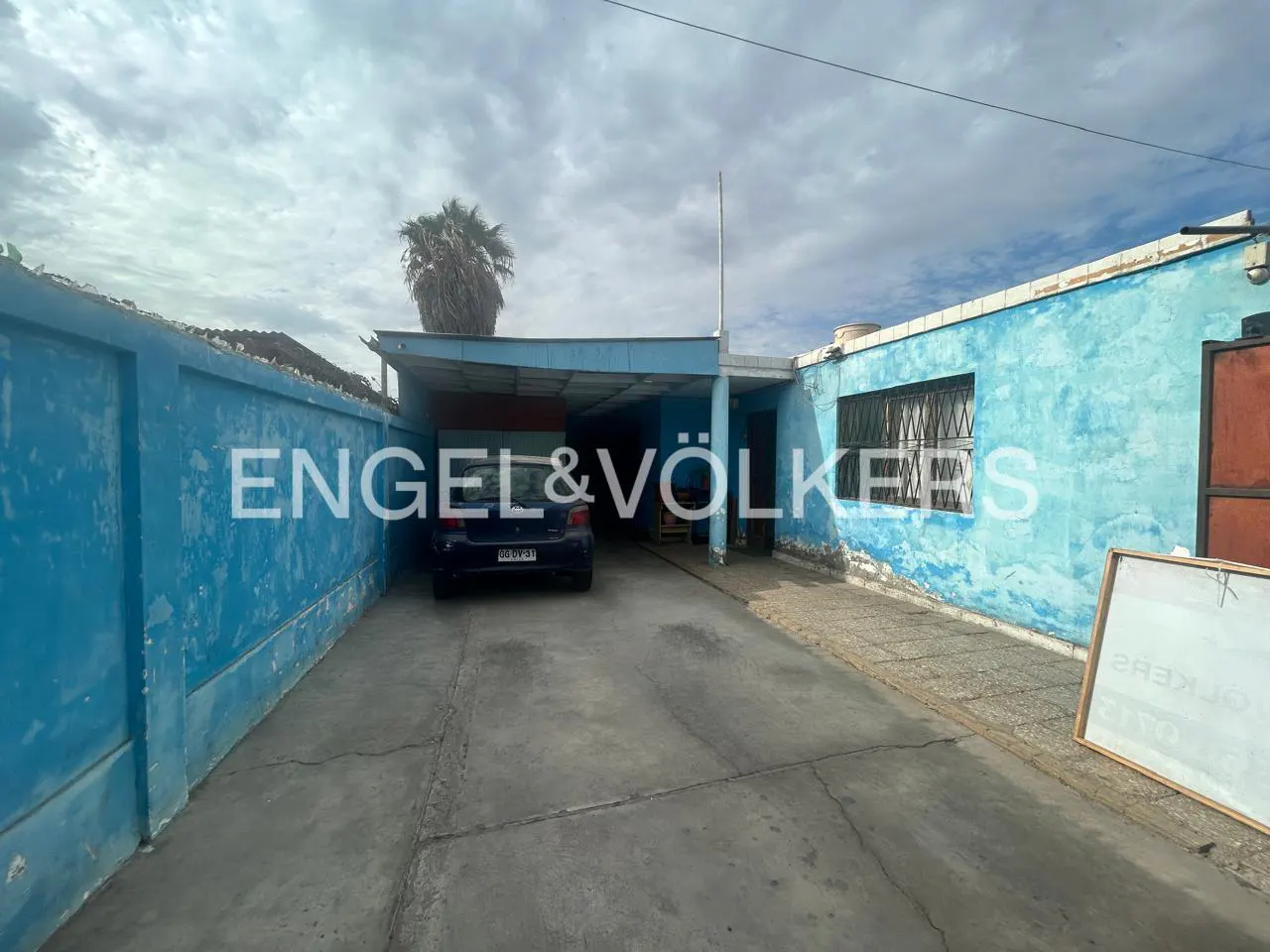 Exterior of a blue house with a car parked in the driveway under a carport. The sky is cloudy.