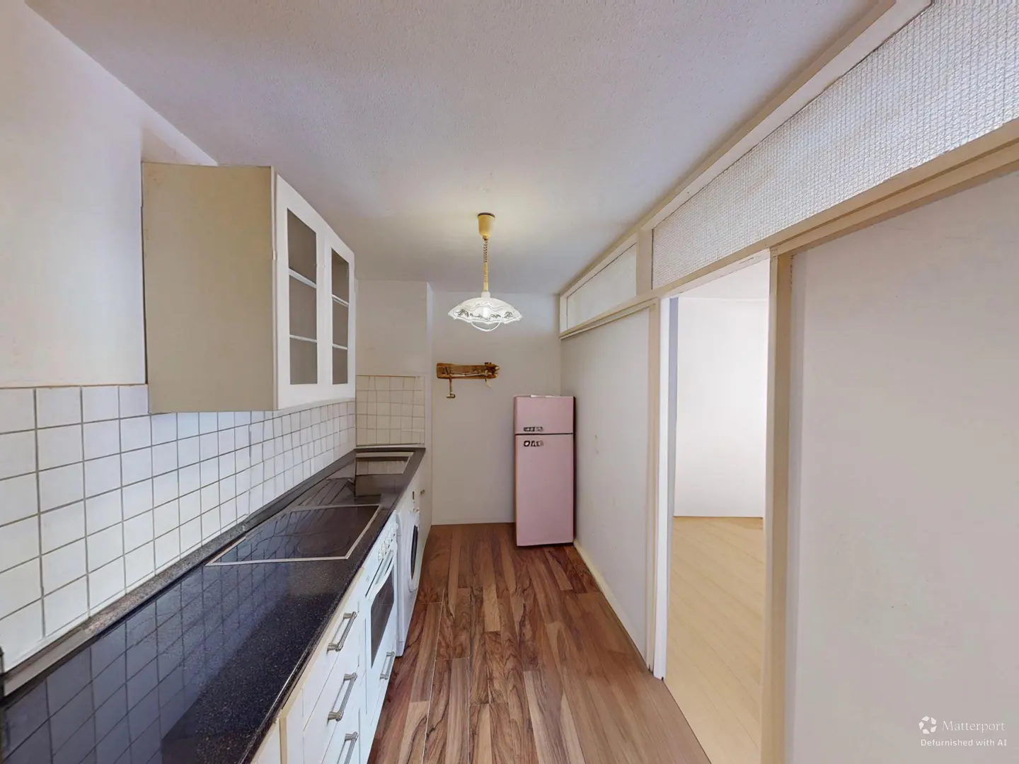 A kitchen with white cabinets, black countertops, and a pink refrigerator. Wood floors run throughout the space.
