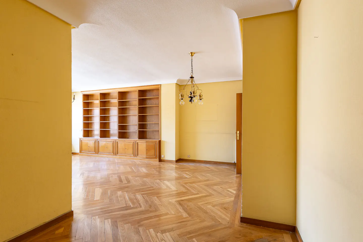 A view into a yellow room with a wood floor, built-in bookshelf, and chandelier.