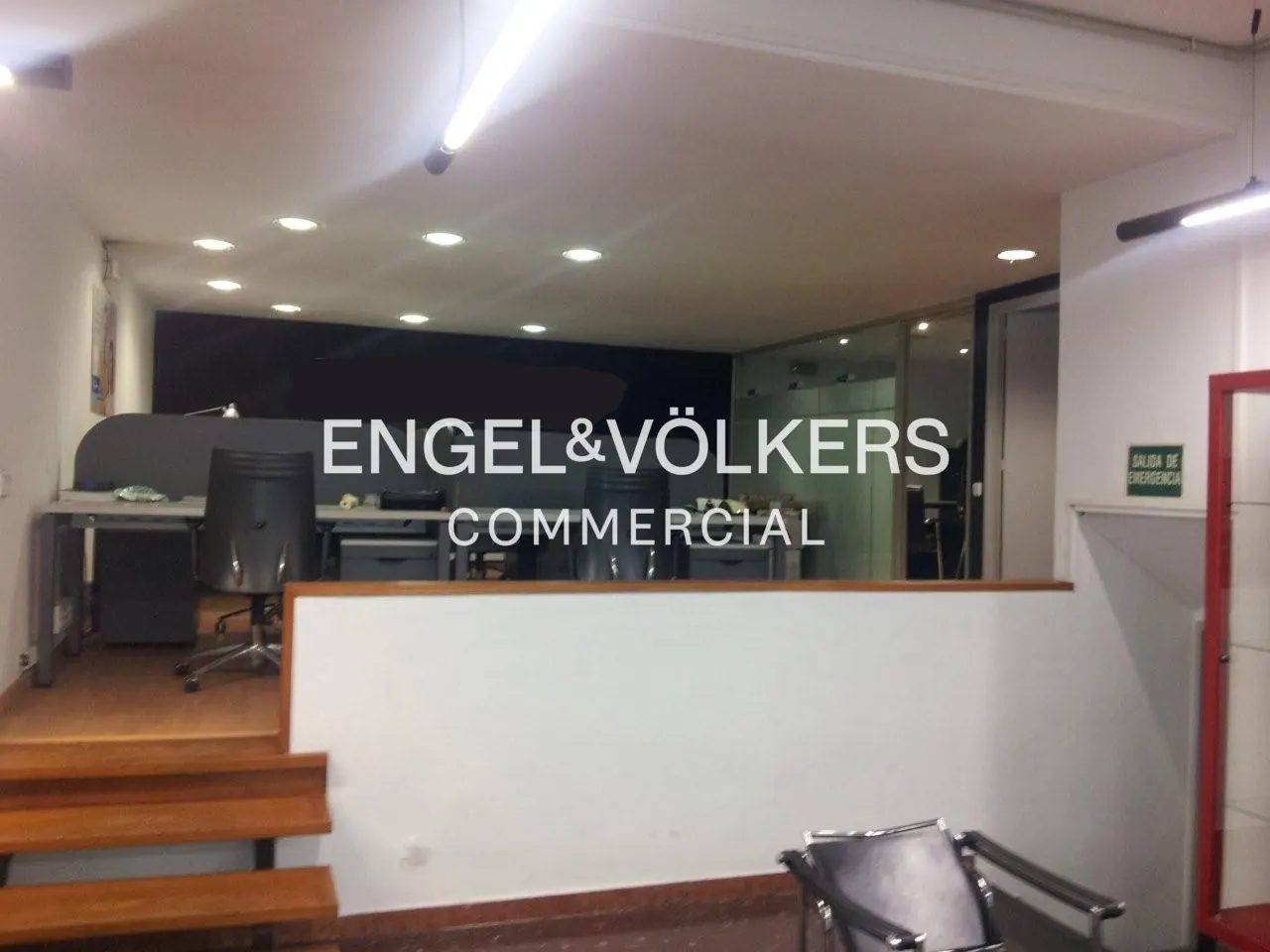 Interior view of Engel & Völkers Commercial office with desks, chairs, and a glass-enclosed area. The space is brightly lit with white walls.