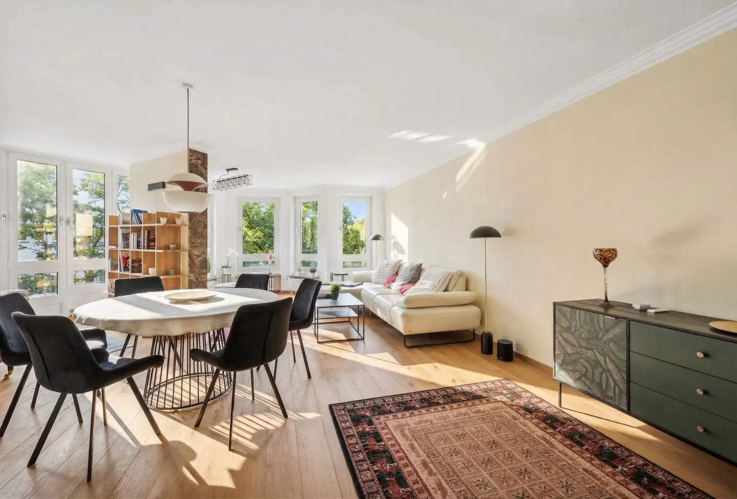 Bright living room with wood floors, a white sofa, a round dining table with black chairs, and a green cabinet.