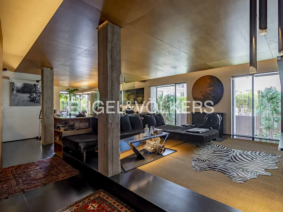 Modern living room with concrete pillars, black sofa, zebra print rug, and warm lighting under a wooden ceiling.