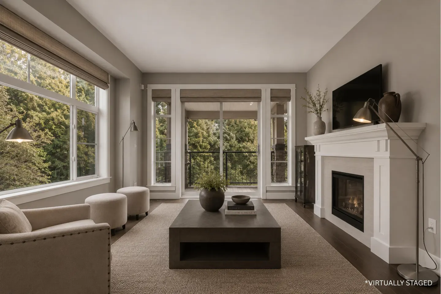 Virtually staged living room with a fireplace, dark coffee table, beige armchairs, and large windows overlooking trees.