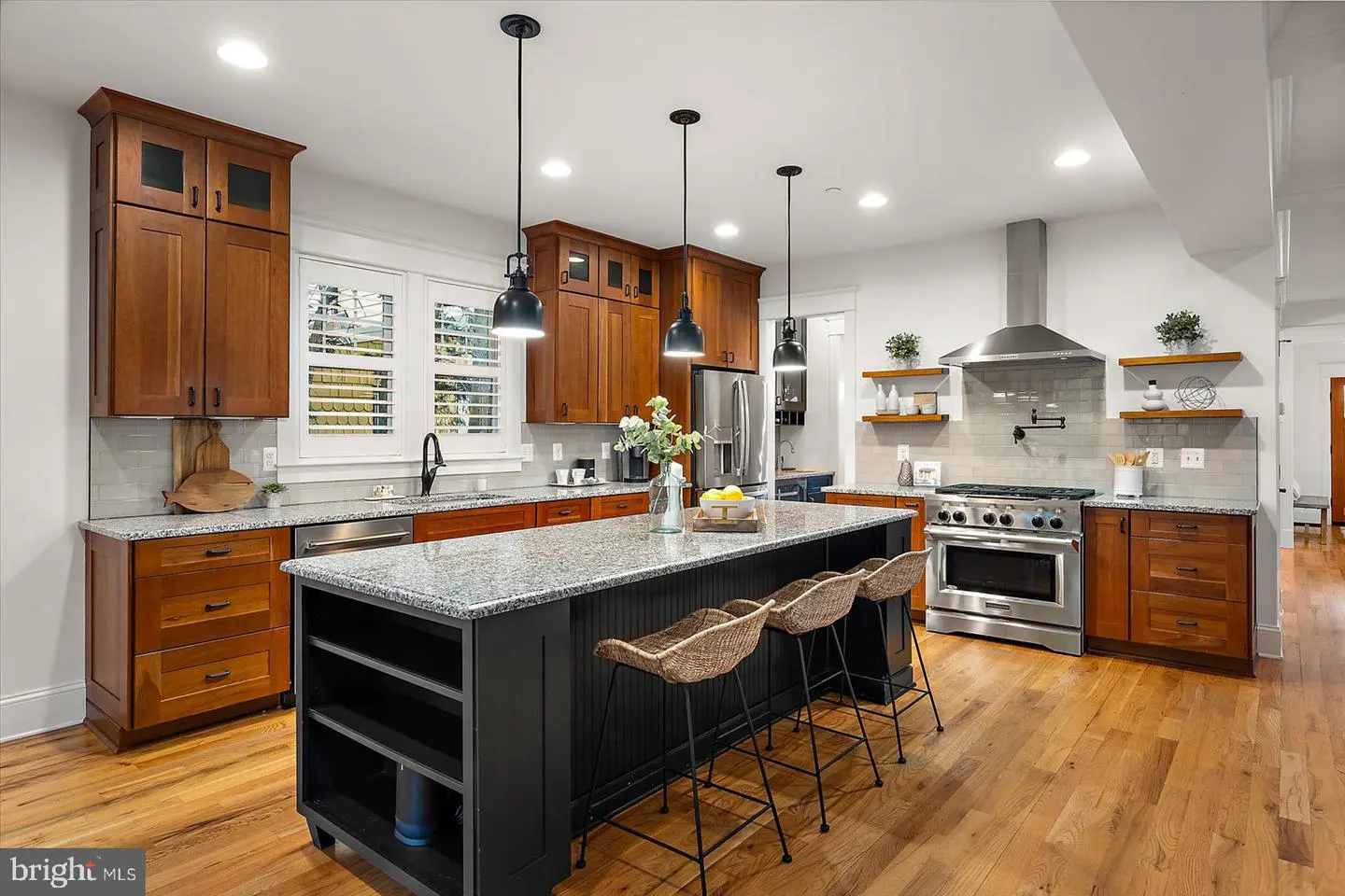 A modern kitchen with wood cabinets, a black island with granite countertop, and three woven bar stools.