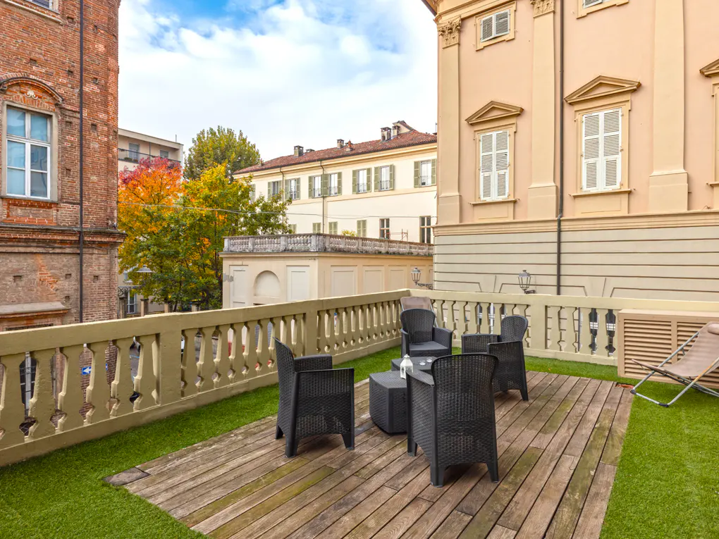 Outdoor patio with black wicker furniture on a wooden deck, surrounded by a stone balustrade and buildings.