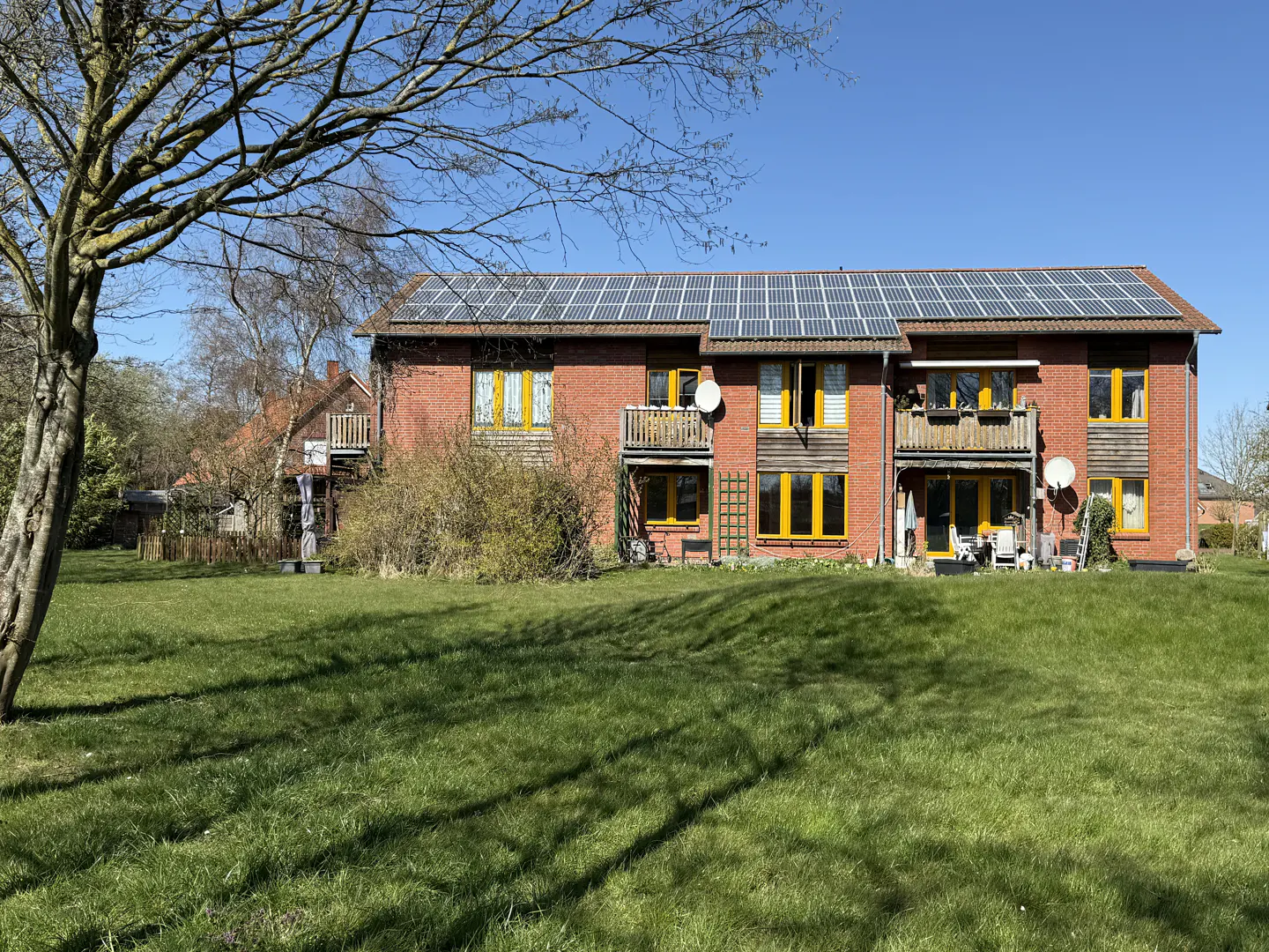 Brick apartment building with solar panels on the roof, yellow window frames, and a green lawn in front.