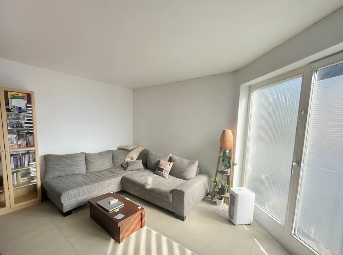 Living room with a gray sectional sofa, a dark wood coffee table, and a bookcase. A large window lets in natural light.