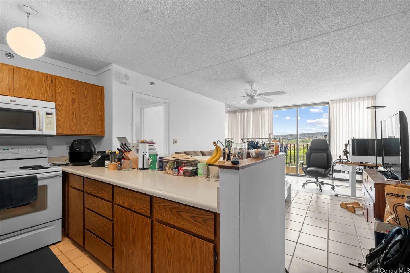 Kitchen with wood cabinets, white appliances, and a breakfast bar overlooking a living area with a view of the outdoors.