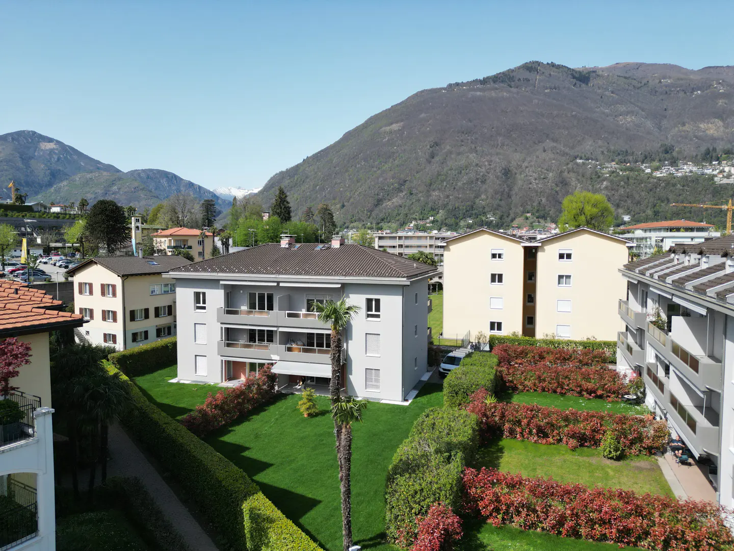 A three-story gray apartment building with balconies, green lawn, and mountain backdrop.
