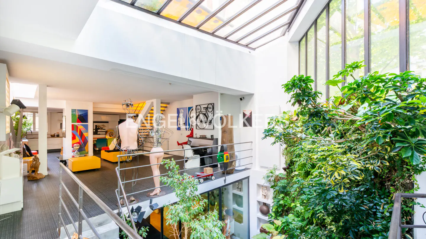 Bright, modern loft with a glass ceiling, indoor plants, and mannequins. Yellow sofas and colorful artwork add to the eclectic decor.