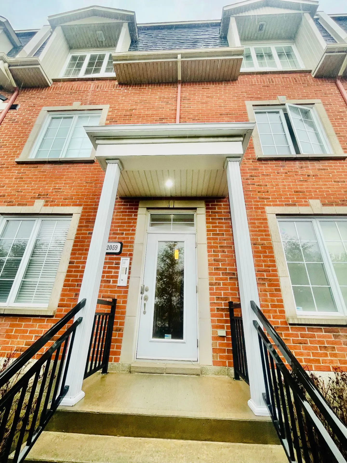 Low angle view of a red brick townhouse with white trim, black railings, and a white front door with the number 2059.