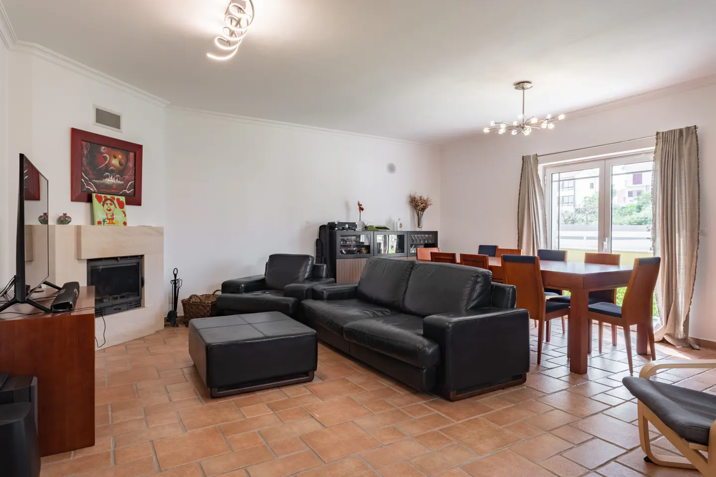 A living and dining area with black leather furniture, a fireplace, and a dining table with chairs on a terracotta tile floor.