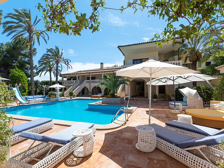 Luxury villa with a pool, lounge chairs, and palm trees under a sunny blue sky.