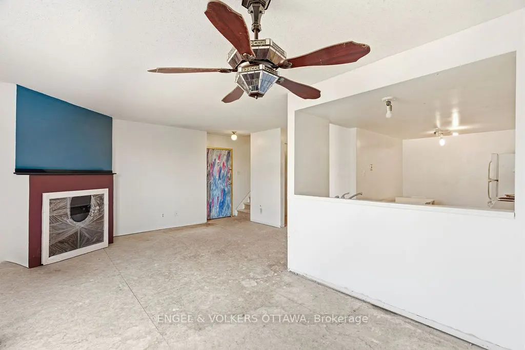 A living room with a blue accent wall, a fireplace, and a view into the kitchen through a cut-out in the wall. A ceiling fan hangs above.