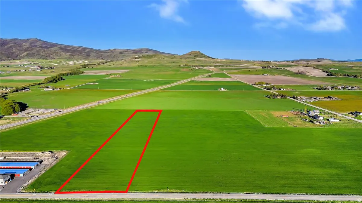 Aerial view of a green field outlined in red, with mountains in the background under a blue sky.