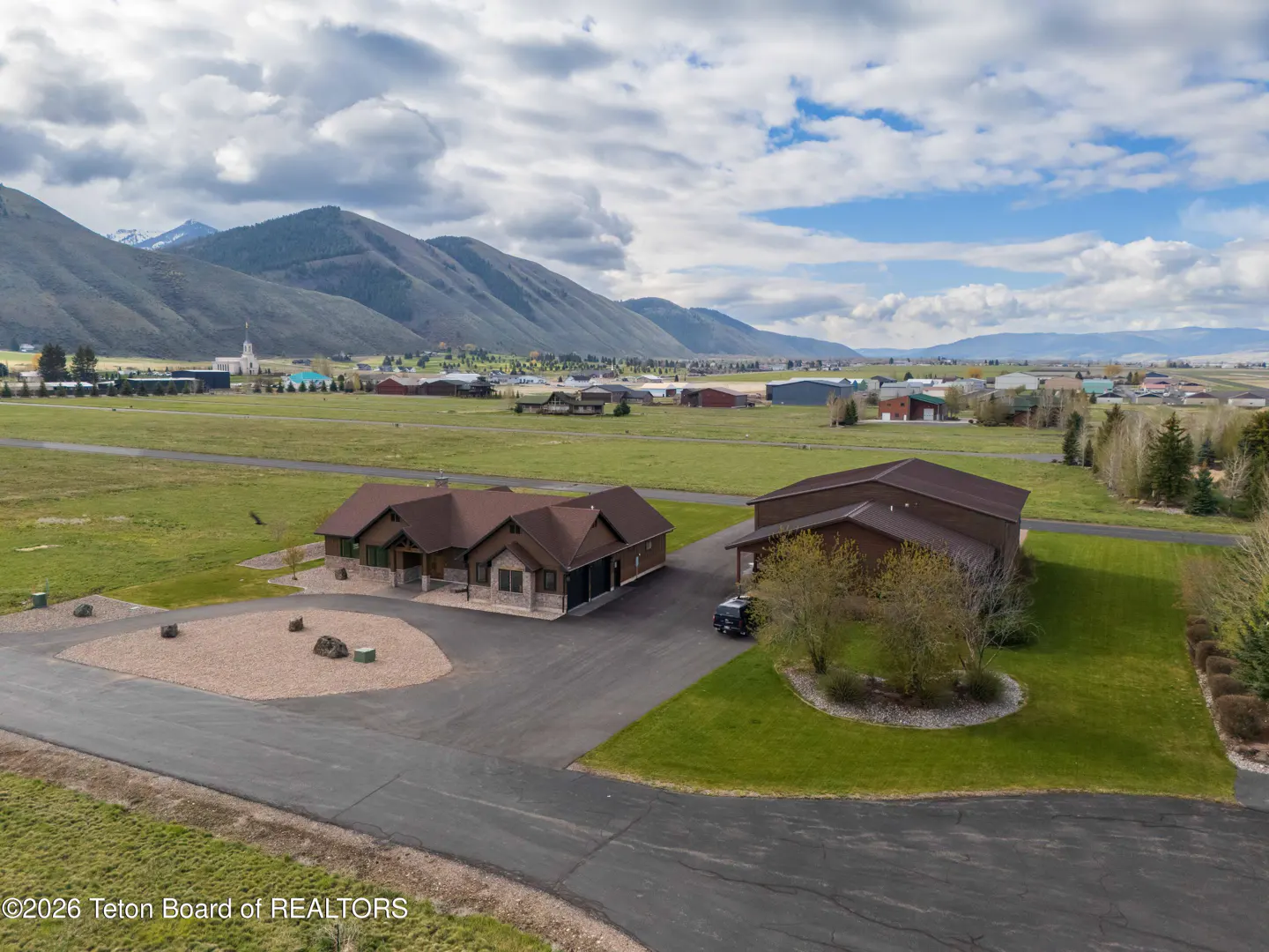 Aerial view of a brown house and garage with mountains and a town in the background.