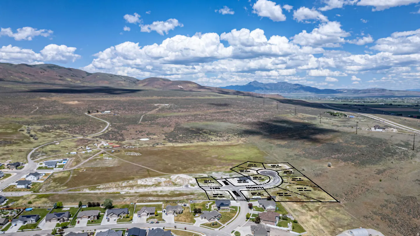 Aerial view of a residential land development plot outlined in black, set against a backdrop of mountains and blue sky.